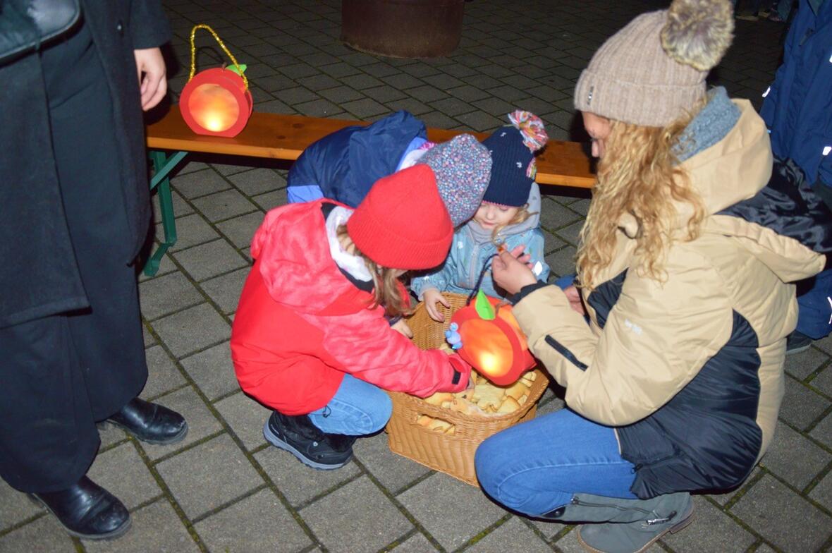 Kinder im Kindergarten Wirbelwind basteln mit einer Betreuerin Laternen und snacken Plätzchen.