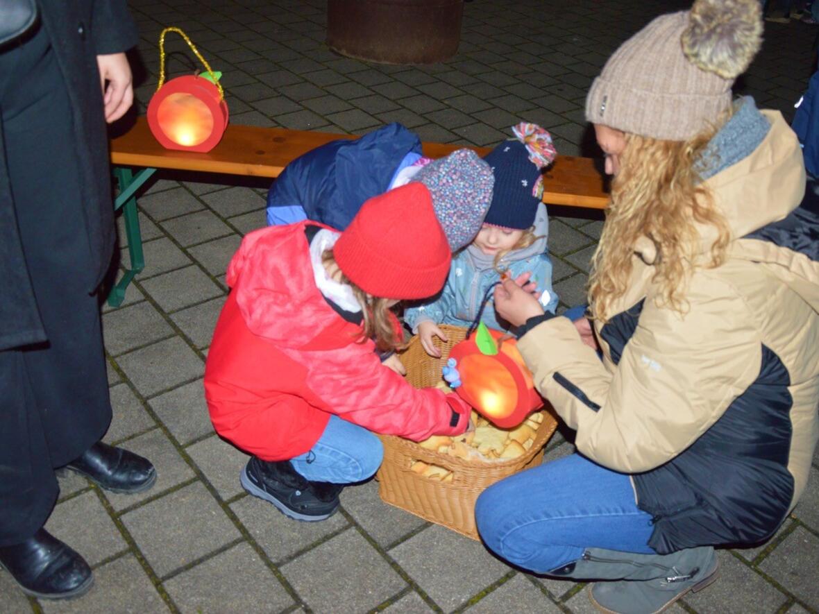 Kinder im Kindergarten Wirbelwind basteln mit einer Betreuerin Laternen und snacken Plätzchen.