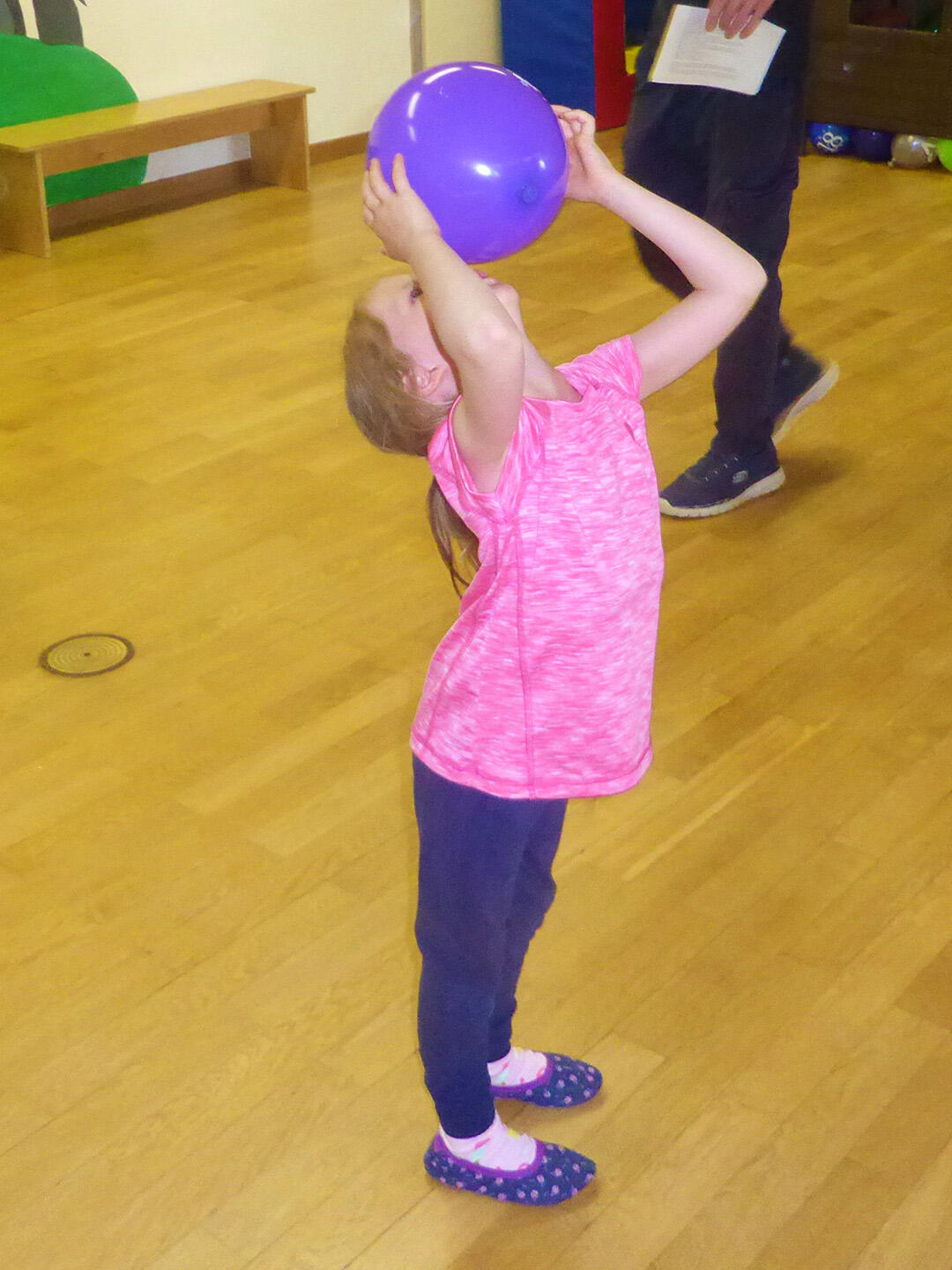 Ein Mädchen hebt einen lila Ball über den Kopf, während sie in einem Spielraum steht.
