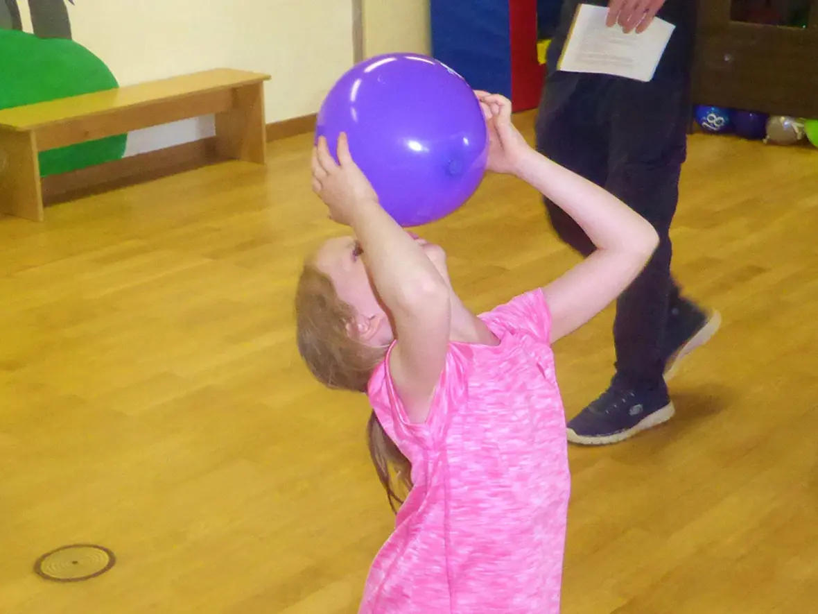 Ein Mädchen hebt einen lila Ball über den Kopf, während sie in einem Spielraum steht.