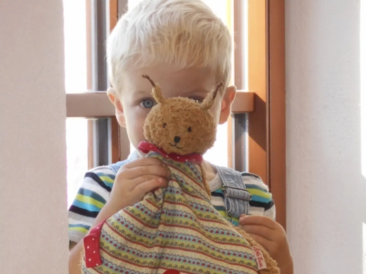 Ein blondes Kind hält eine bunte Stofffigur in Form einer Schnecke in der Hand.