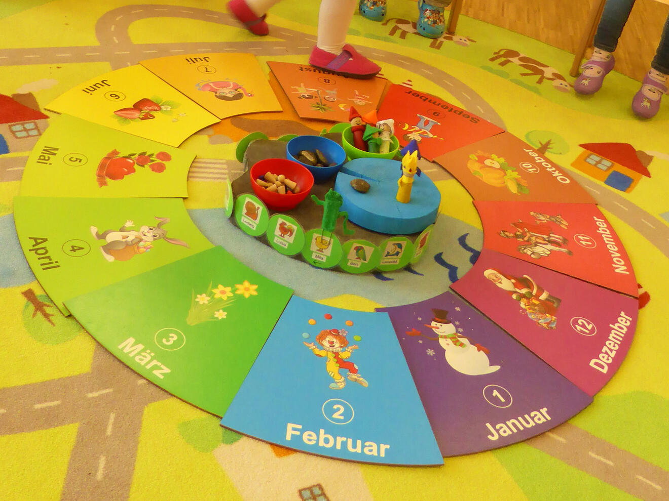 Ein bunten Förderkreis mit Monaten, verziert mit Illustrationen und einem zentralen Spielelement im Kindergarten.