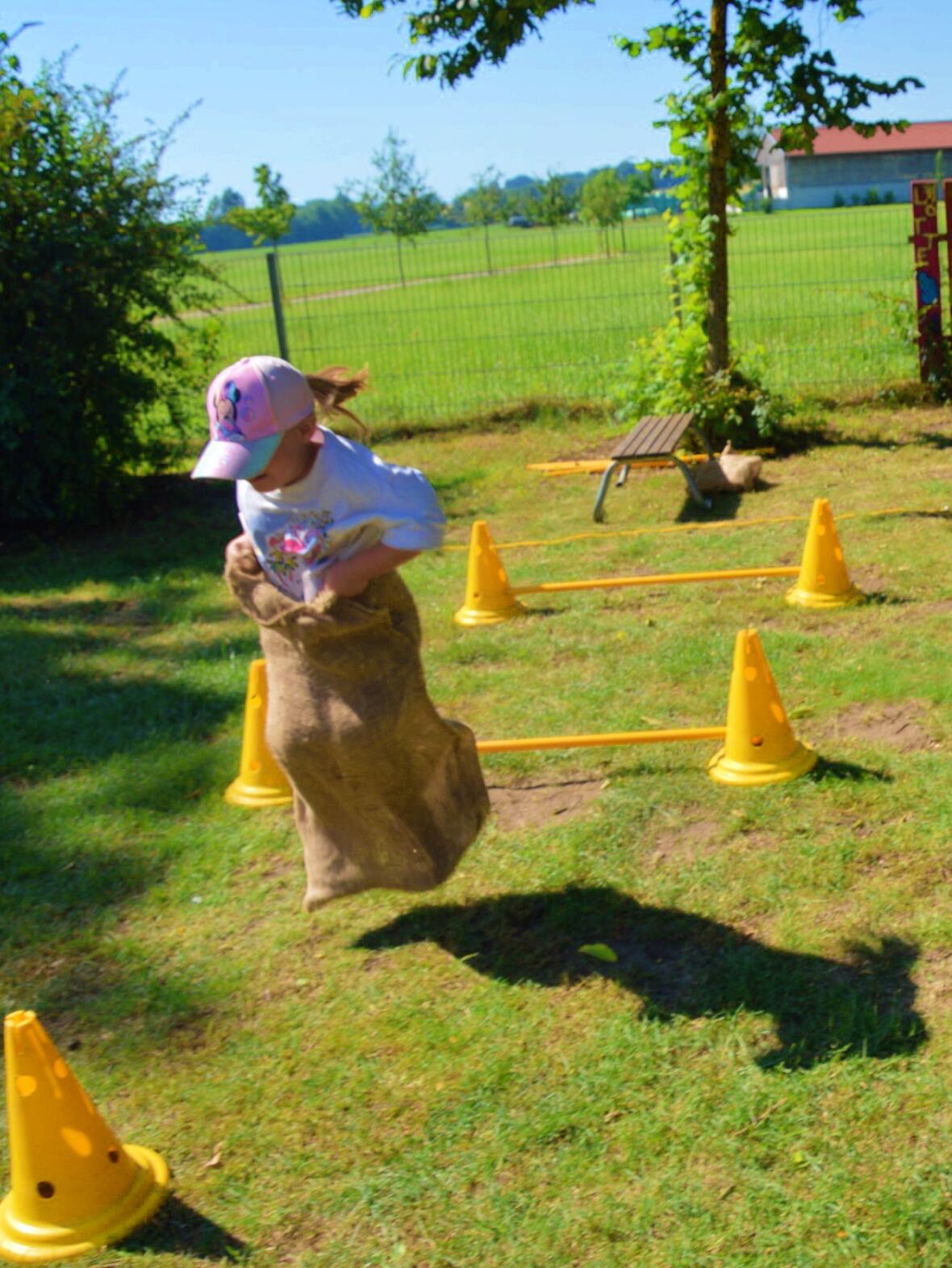 Mädchen springt im Sack über Hürden auf dem grünen Spielplatz.