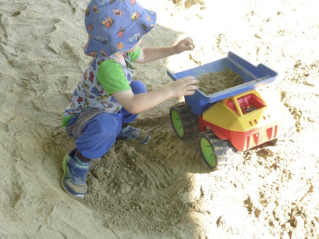 Kind spielt im Sandkasten mit einem roten und blauen Sandspielzeug.