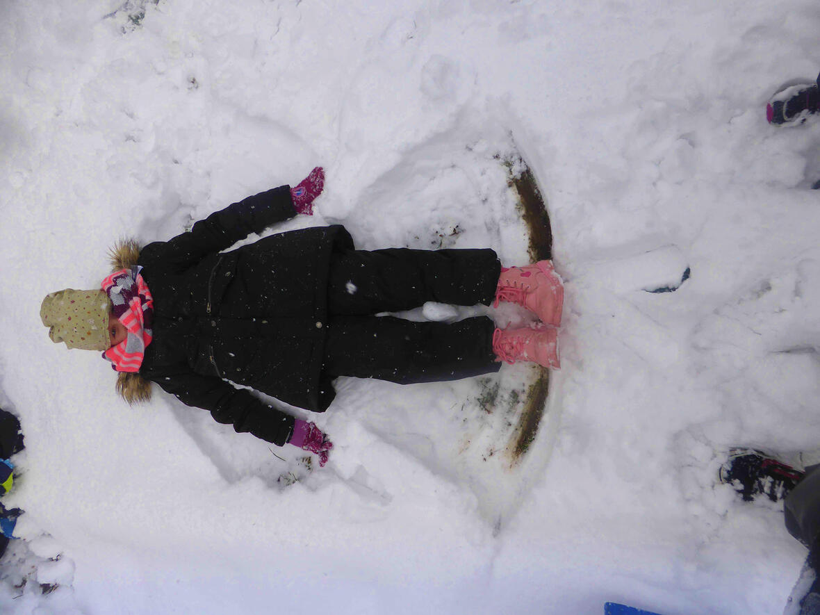 Ein Kind liegt im Schnee und hat einen Schneeengel geformt, umgeben von unberührtem Schnee.