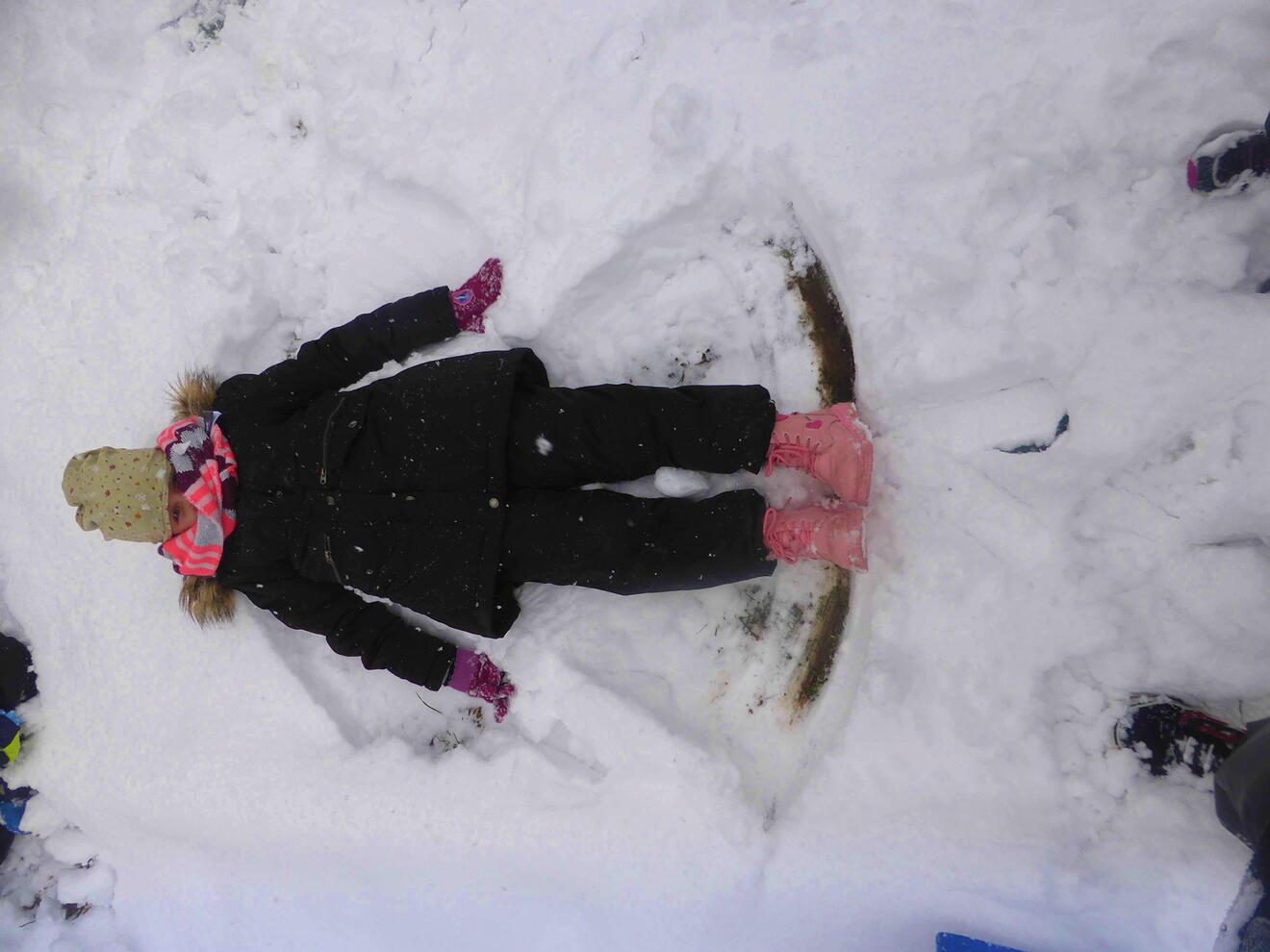 Ein Kind liegt im Schnee und hat einen Schneeengel geformt, umgeben von unberührtem Schnee.