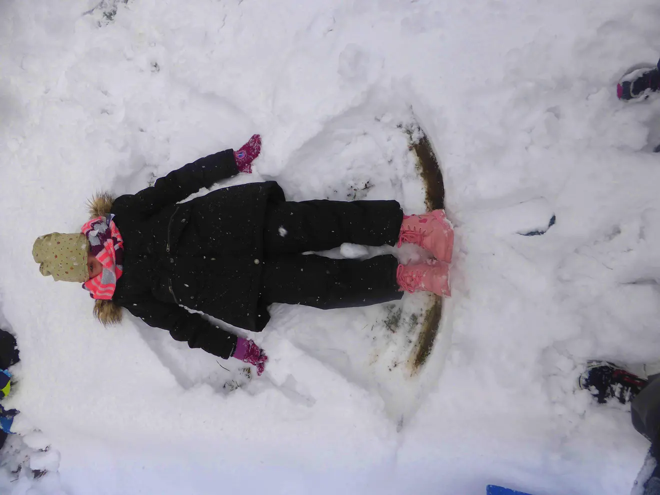 Ein Kind liegt im Schnee und hat einen Schneeengel geformt, umgeben von unberührtem Schnee.