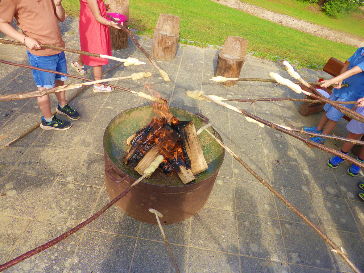 Kinder rösten Stockbrot über einem offenen Feuer in einem Freizeitbereich.