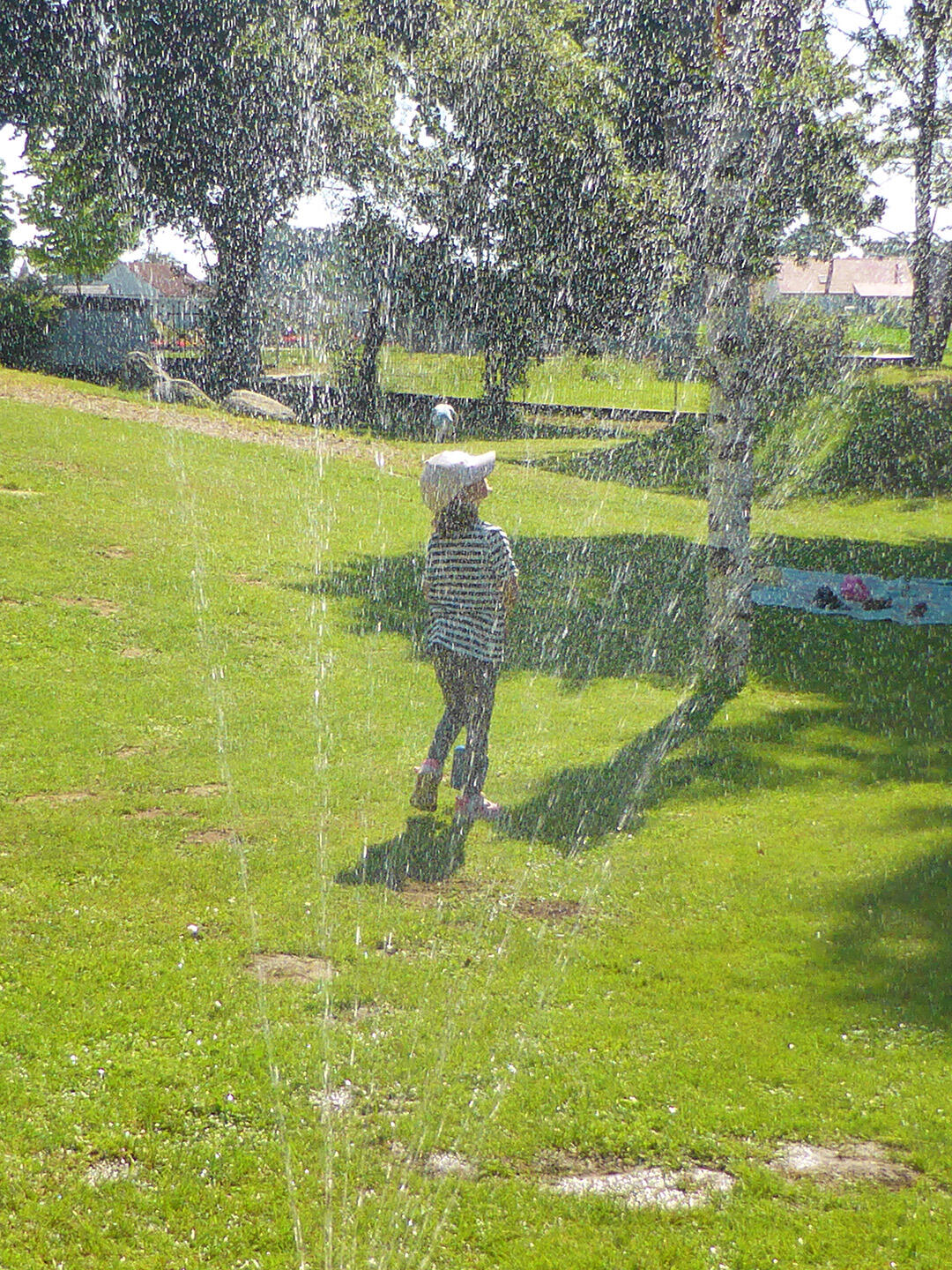 Ein Kind mit einem weißen Hut spielt im Sprühnebel eines Wasserspenders im Park.